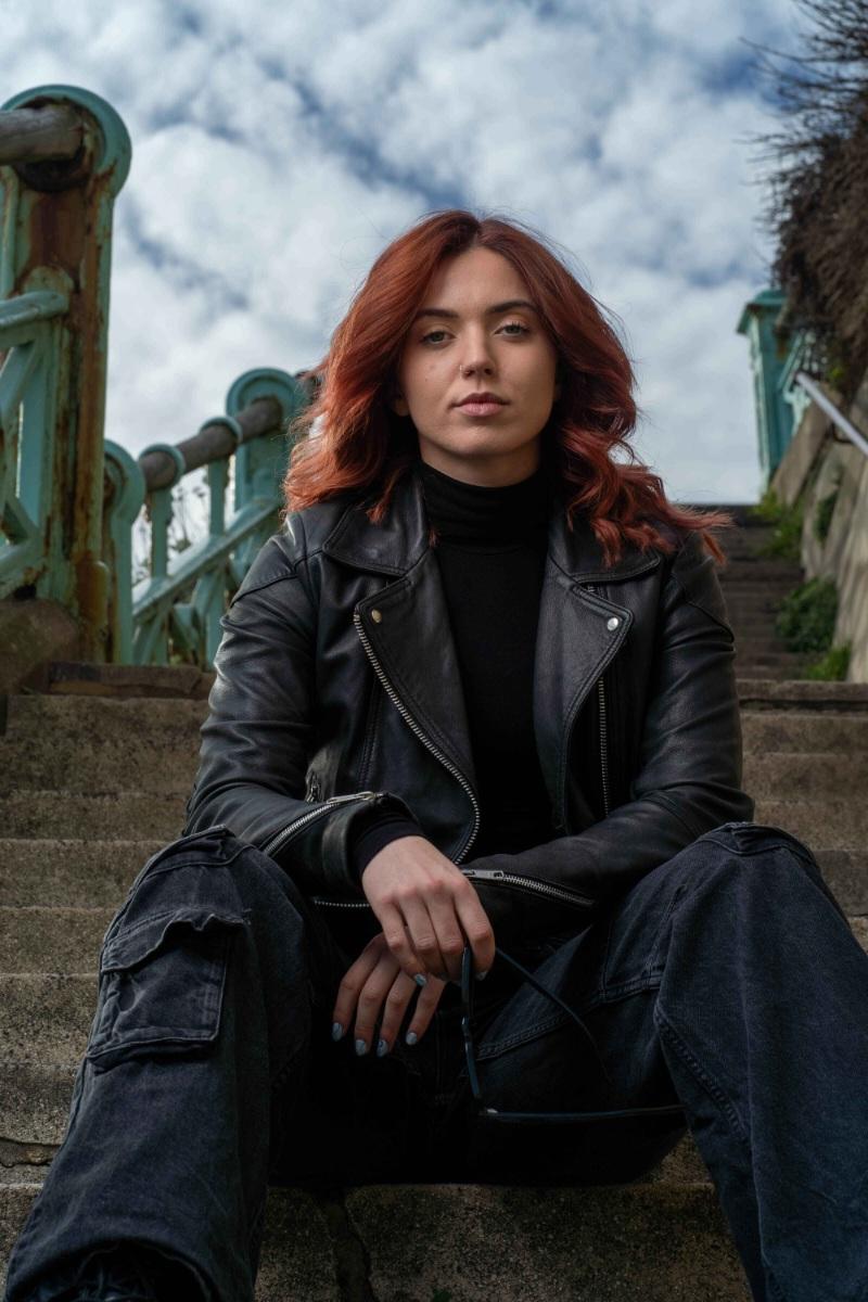 Portrait of a red-haired woman in a black leather jacket, seated on outdoor steps